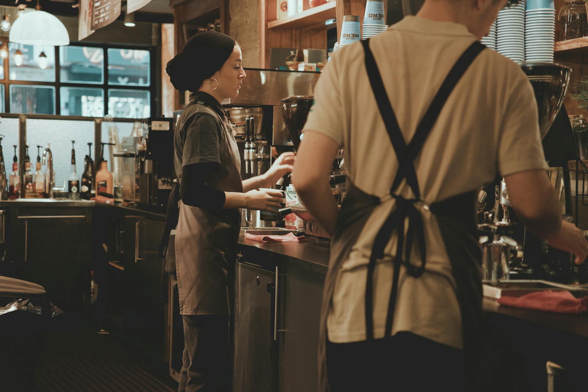 Barista Belgesi Nasıl Alınır? 1 Baristas at work in a cozy café, using coffee machines to prepare drinks.
