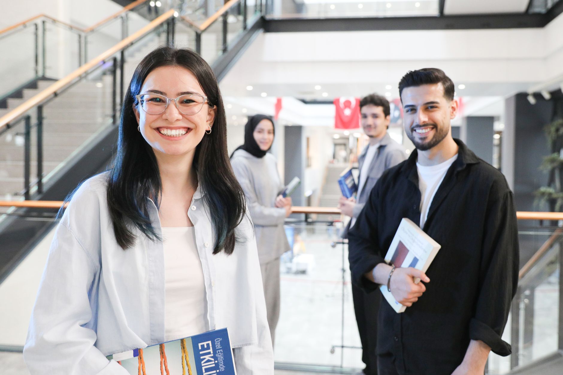 KVKK Eğitimi Fiyatları 2026 1 A diverse group of students in a modern indoor mall setting, smiling and holding books.