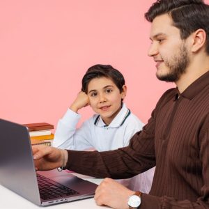 Türkiye'nin Yalova şehrinde, pembe bir arka plan önünde bir öğretmen, bir öğrenciye dizüstü bilgisayarla ders çalışmasına yardımcı oluyor.