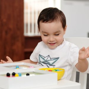 A cheerful child engaged in play with colorful beads indoors, expressing delight and curiosity.