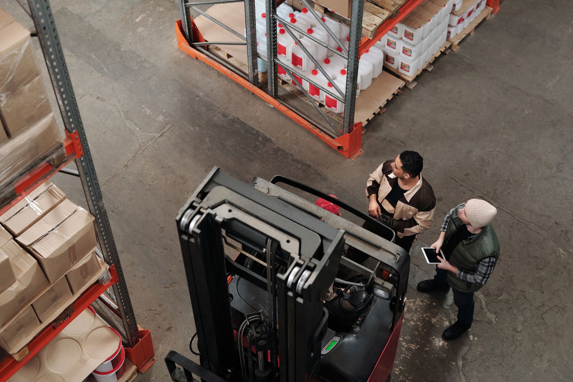 PERSONEL YÜK YÜKSELTİCİ BİLGİLENDİRME EĞİTİMİ Sertifikası 1 Two workers in a warehouse discussing logistics near a forklift captured from above.