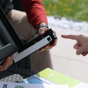 Close-up of two people examining an aluminum window frame outdoors.