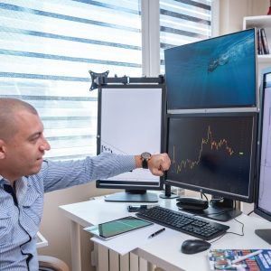 A trader analyzing market trends on multiple monitors at an indoor office desk.