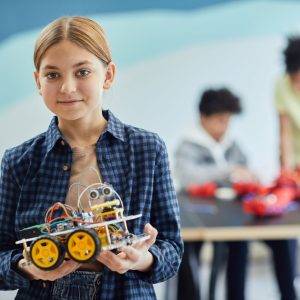 Girl proudly displays her robotics project in a classroom setting.