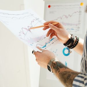 A man analyzing stock market charts with a pen, holding a paper report indoors.