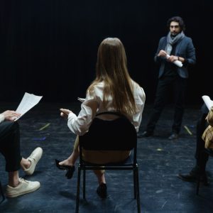 Group of actors in rehearsal with director, practicing for a theater performance.