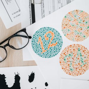 Close-up of color blindness test sheets with eyeglasses on a wooden table.