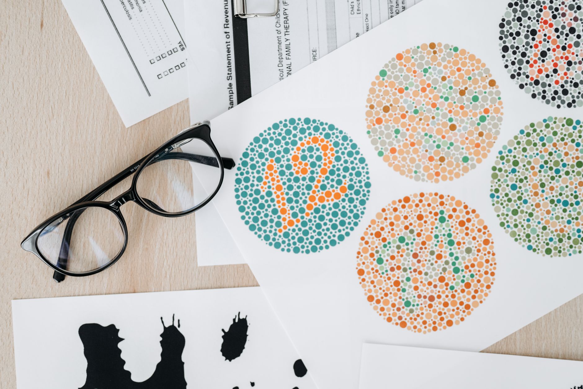 YETİŞKİN PSİKOTERAPİSİNDE 12 TEST EĞİTİMİ Sertifikası 1 Close-up of color blindness test sheets with eyeglasses on a wooden table.