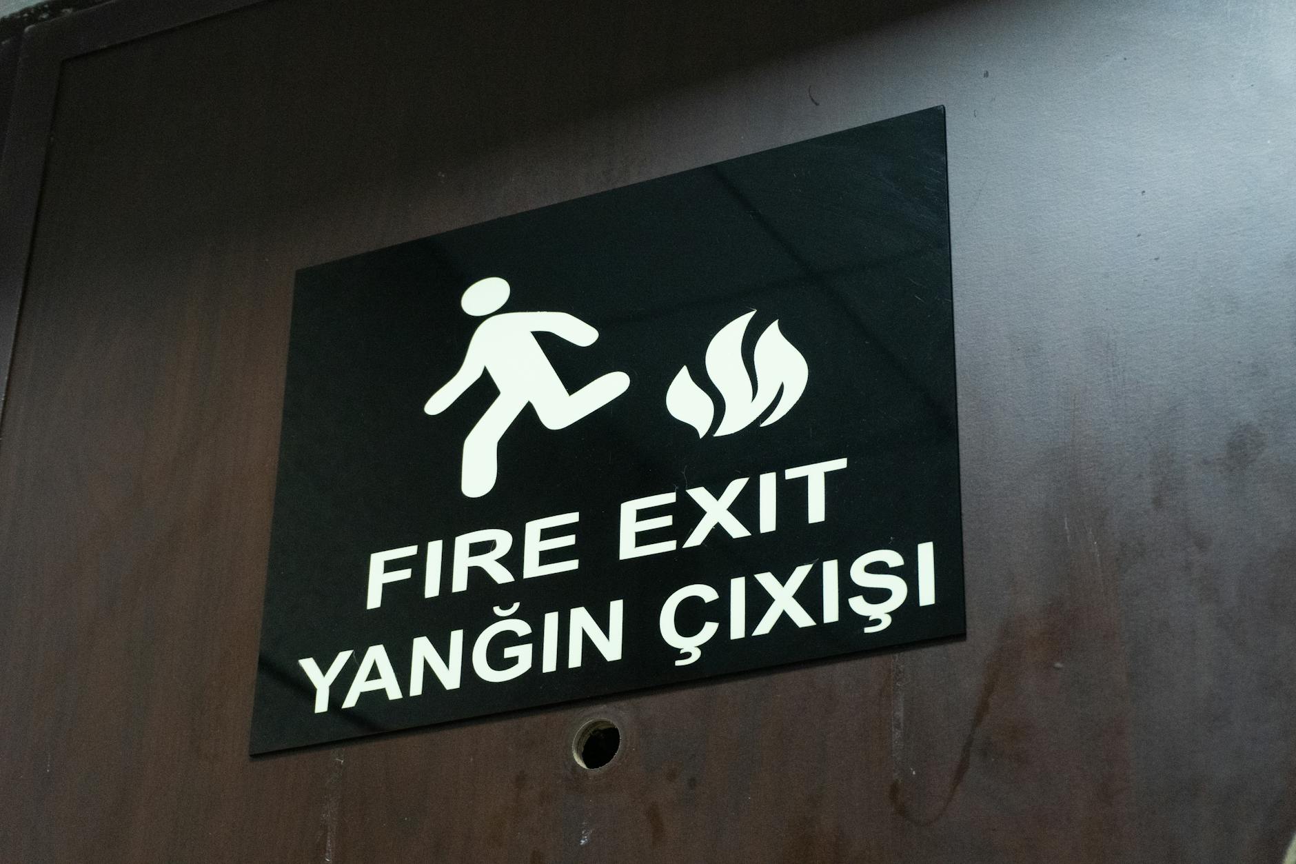 Yangın Eğitici Eğitimi Seviye - 1 Sertifikası 1 Bilingual fire exit sign displaying English and Turkish text on a wooden door.