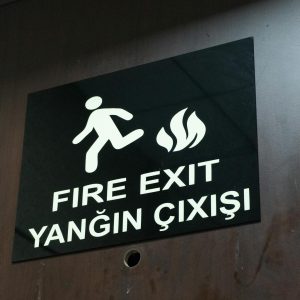 Bilingual fire exit sign displaying English and Turkish text on a wooden door.