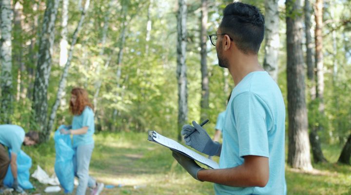 ISO 14001 Eğitimi Kimler İçin Uygundur? Çevre Yönetimi Sertifika Rehberi 4 Volunteers collect litter in a forest, showcasing teamwork and environmental care.