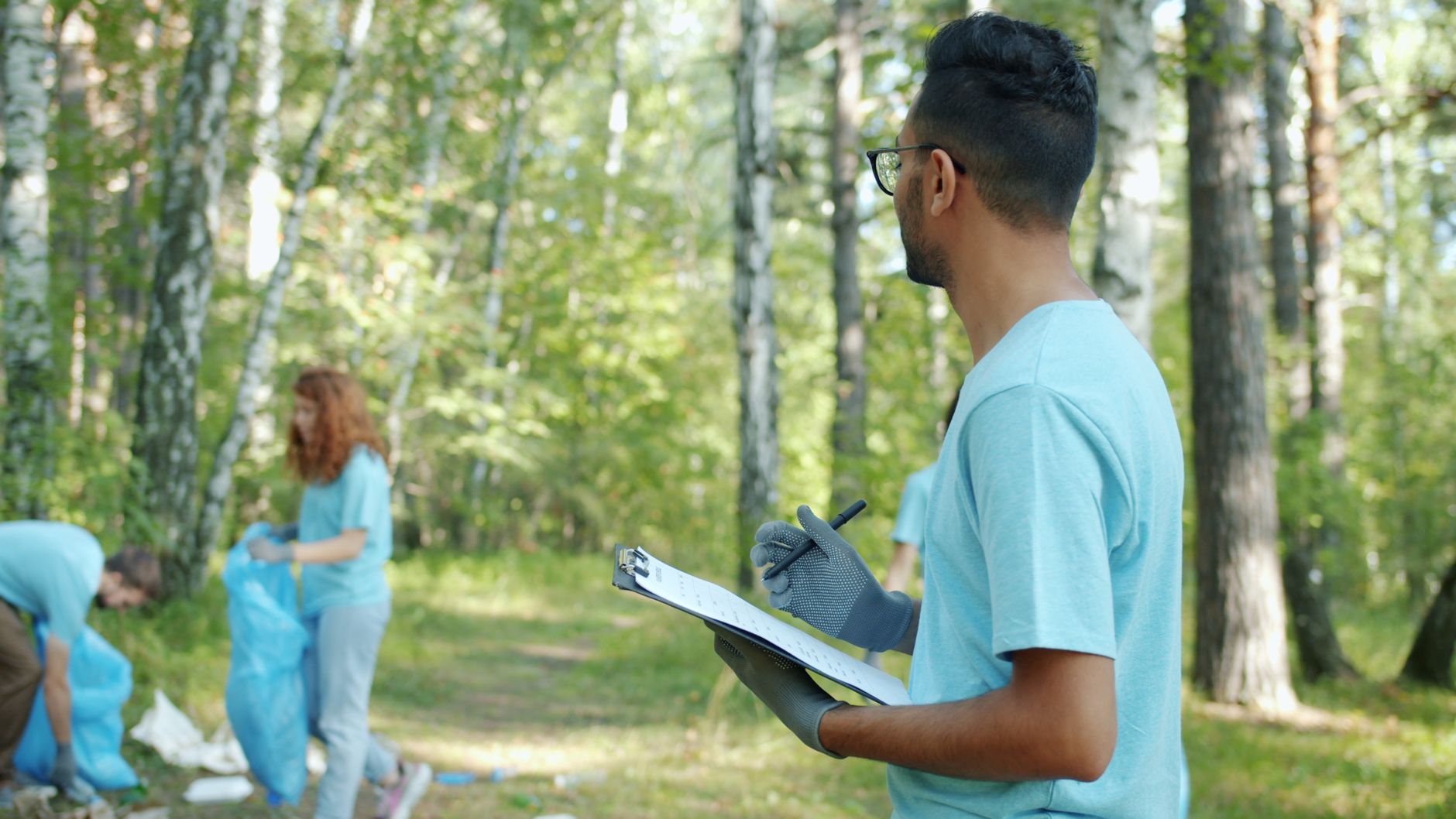 ISO 14001 Eğitimi Kimler İçin Uygundur? Çevre Yönetimi Sertifika Rehberi 1 Volunteers collect litter in a forest, showcasing teamwork and environmental care.
