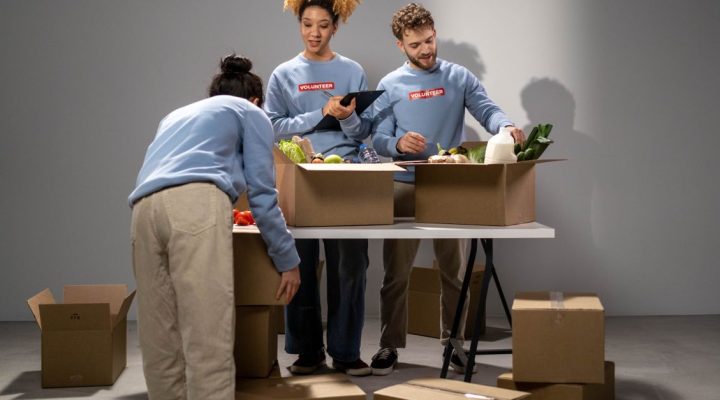 ISO 26000 Eğitimi Kimler İçin Uygundur? Sosyal Sorumluluk Rehberi 1 Üç gönüllü, kutulara yiyecek bağışlarını organize ediyor, takım çalışması ve toplumsal destek gösteriyor.