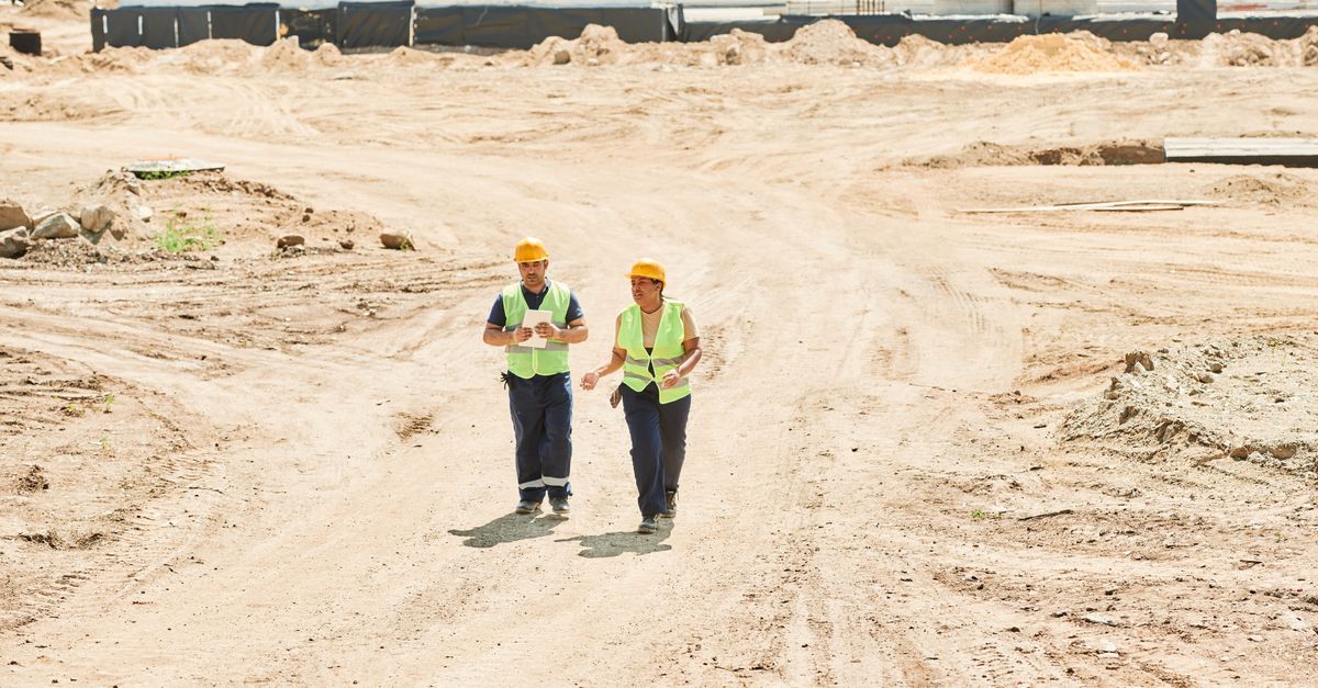 İç Tetkikçi Ne İş Yapar? ISO 19011’e Göre Görev ve Sorumlulukları 1 Açık bir gökyüzü altında güvenlik ekipmanlarıyla yürüyen iki işçi inşaat alanında.
