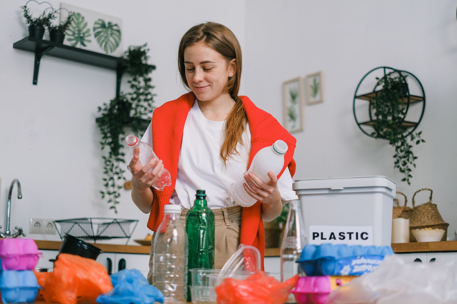 Plastik İşleme Sertifikası Nasıl Alınır? Kimler Katılabilir? 1 Cheerful female in casual clothes standing with plastic bottles in hands while sorting trash in light kitchen in daytime